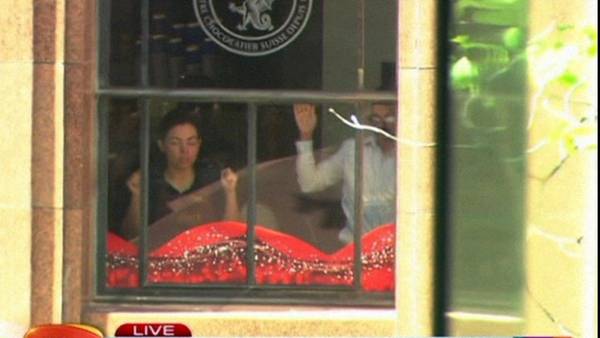 Imagen de TV en donde se ve a dos supuestos rehenes dentro de un café y chocolatería del centro de Sidney. (AP)