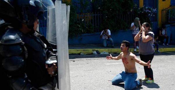 Un joven con sangre en su pecho se arrodilla frente a policías después de que el estudiante de 14 años, Kluiver Roa, fuera asesinado en una protesta en San Cristóbal, Caracas