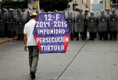 Un hombre camina, con un cartel en la espalda, en frente de los guardias nacionales durante una marcha contra el gobierno del presidente de Venezuela, Nicolás Maduro
