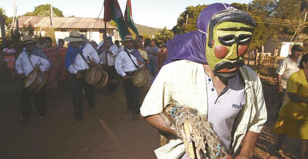 Escena del desfile del Cabildo Indígena precedido por tamboritas y el abuelo con su máscara de toco