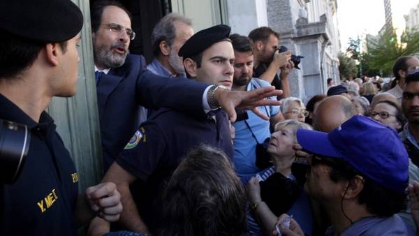 Tranquilidad. Un gerente del Banco Nacional de Grecia, cercado por policías, pide calma a los jubilados que intentan entrar al edificio en Atenas. AP