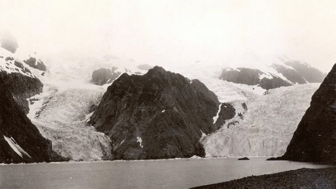 La fotografía de 1909 muestra al Glaciar Holgate, de marea en la cabecera del fiordo, con el Pequeño Glaciar de Holgate, uno de sus antiguos afluentes , situado a su izquierda. No hay vegetación presente