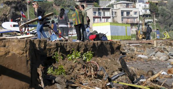 Personas caminan por la playa al lado de tiendas destruidas por las olas después de que un terremoto de 8,4 grados sacudiera Chile
