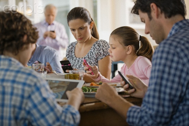 Family including kids (8-9) texting at dinner table --- Image by © Hiya Images/Corbis