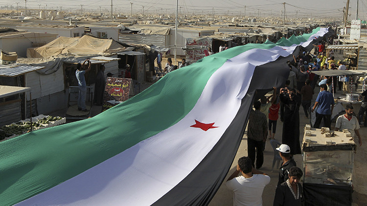 Decenas de refugiados sostienen una gran bandera de la oposición siria en un campamento de Mafraq, Jordania