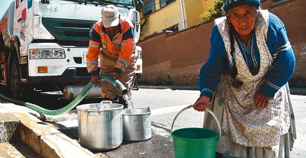 Una persona de la tercera edad intenta cargar agua para llevar a su casa, en una zona alta de La Paz