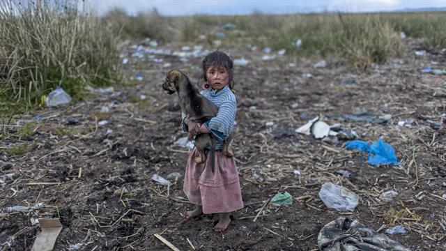 Melinda Quispe camina sobre la basura derramada a orillas del lago Titicaca, con su perro en brazos , en Kapi Cruz Grande, en la región de Puno en Perú