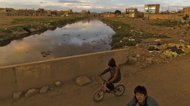 Niños en bicicleta sobre un puente del río Torococha cerca de una planta de tratamiento de residuos municipales con agua que desemboca en el Lago Titicaca, en Juliaca, en la región de Puno, Perú.