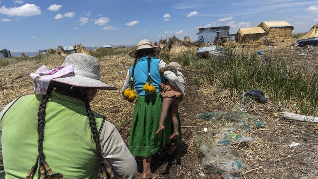 Una mujer lleva a su bebé camino a su casa en Kapi Cruz Grande, una aldea en las orillas llenas de basura del Lago Titicaca en la región de Puno en Perú