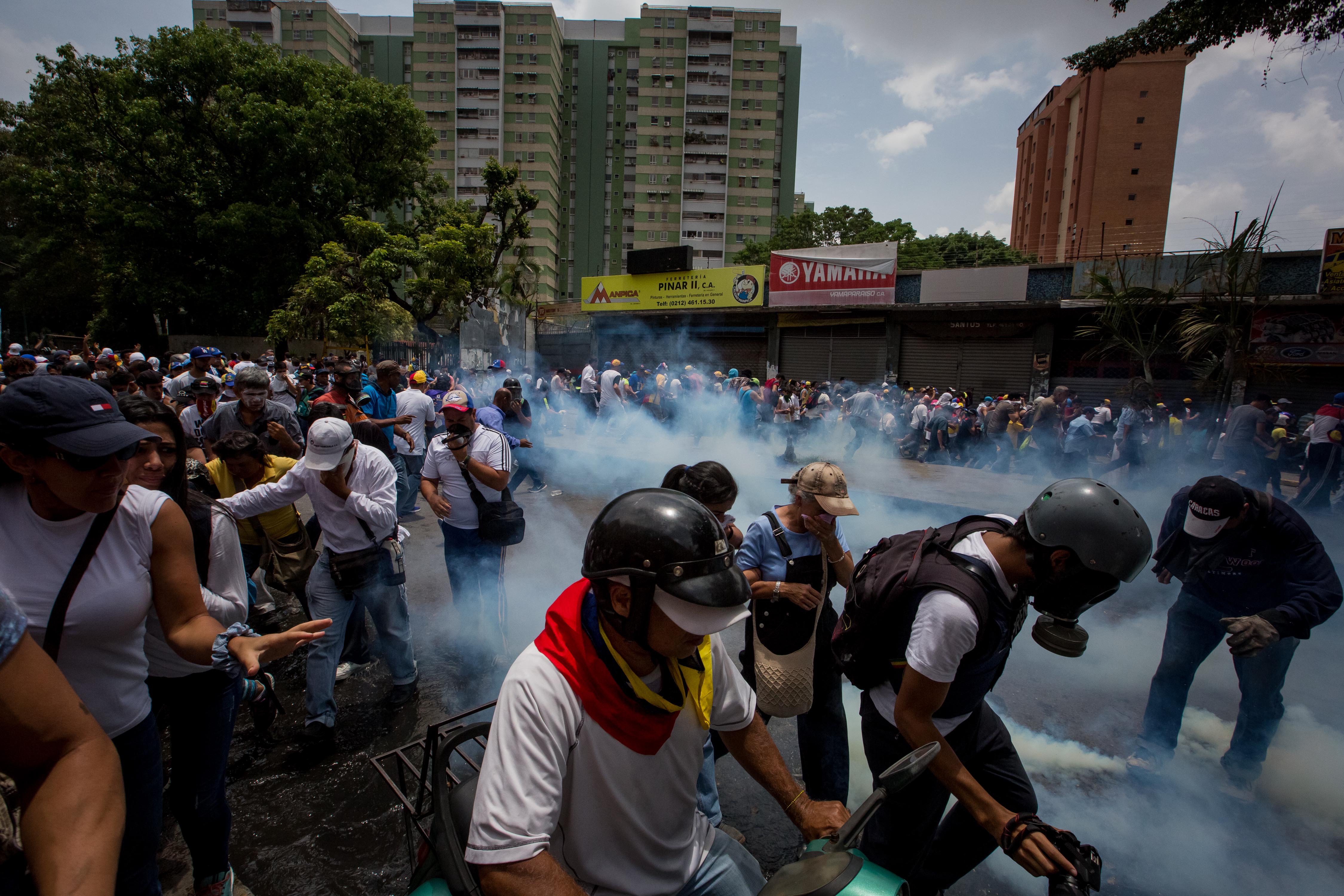 CAR012. CARACAS (VENEZUELA),19/04/2017 - Manifestantes se protegen de los gases lacrimógenos durante una protesta en contra del Gobierno venezolano hoy, miércoles 19 de abril de 2017, en Caracas (Venezuela). La policía disolvió hoy con gases lacrimógenos una de las marchas opositoras en el centro de Caracas que pretendía llegar a la sede de la Defensoría del Pueblo, mientras que desde otra de las concentraciones antichavistas en esa zona de la ciudad se reportó una persona muerta. EFE/MIGUEL GUTIERREZ