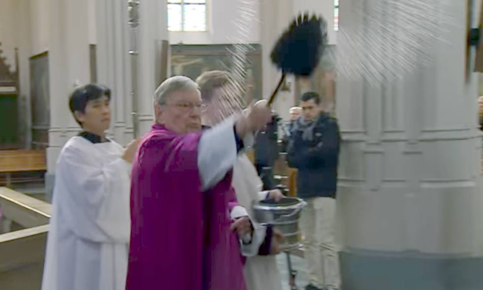 El párroco Jan van Noorwegen rocía con agua bendita el confesionario usado en una de las escenas. La imagen es de un reportaje emitido por la cadena local Omroep Brabant.