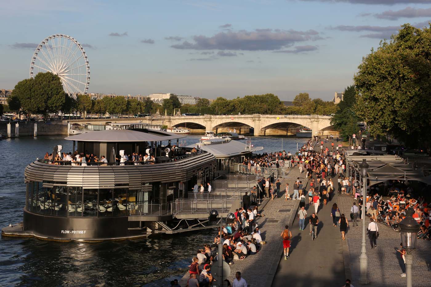 (FILES) This file photo taken on September 01, 2016 shows people having drinks near a barge on the Seine banks and the Grande Roue in Paris. After a decline in 2016 due to the terror attacks in Paris and Nice, tourism in Paris and Ile de France is in much better shape in the first half of 2017, with 1,5 million tourists and 3,3 million overnight stays more than a year ago. / AFP PHOTO / LUDOVIC MARIN