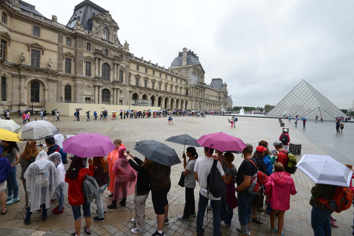 (FILES) This file photo taken on August 08, 2014 shows people queueing under the rain to get in the Louvre Museum in Paris. After a decline in 2016 due to the terror attacks in Paris and Nice, tourism in Paris and Ile de France is in much better shape in the first half of 2017, with 1,5 million tourists and 3,3 million overnight stays more than a year ago. / AFP PHOTO / DOMINIQUE FAGET