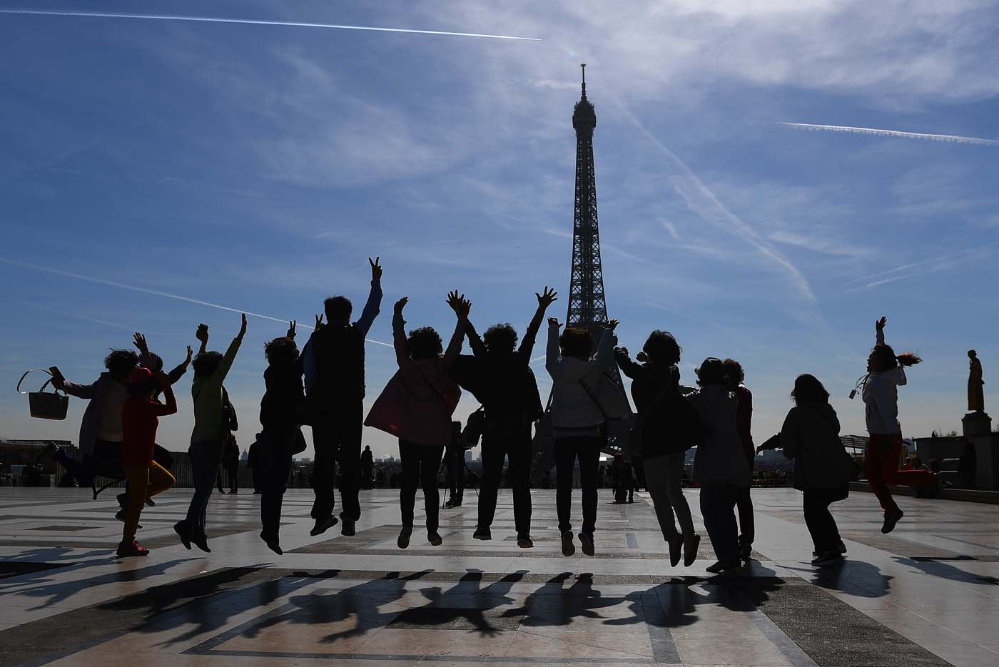 (FILES) This file photo taken on March 30, 2017 shows tourists jumping as they pose for a family photo on the Esplanade du Trocadero near the Eiffel Tower in Paris. After a decline in 2016 due to the terror attacks in Paris and Nice, tourism in Paris and Ile de France is in much better shape in the first half of 2017, with 1,5 million tourists and 3,3 million overnight stays more than a year ago. / AFP PHOTO / GABRIEL BOUYS