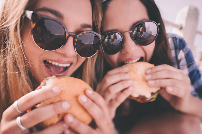 Mejores amigas adolescentes con sendas hamburguesas.
