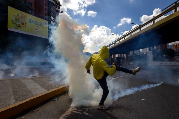 Un manifestante patea una bomba de gas lacrimógeno lanzada por la policía militar chavista (EFE)