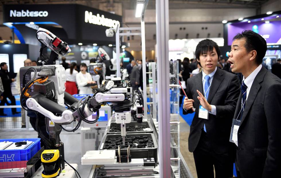 Un par de asistentes observan un robot industrial en una feria de robótica en Tokio. 