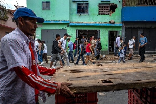 Un grupo de personas caminan frente a una licorera que fue saqueada en horas de la madrugada en el sector La Vega en Caracas (Venezuela). (EFE/Miguel Gutiérrez)