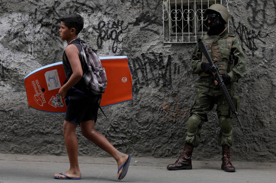 Un joven con una tabla de body-board pasa delante de un soldado desplegado en la favela de Rocinha durante una operación antidroga, en septiembre de 2017. (Reuters)