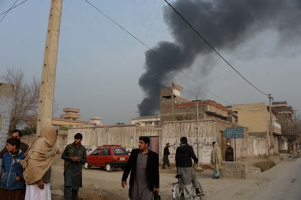 Civiles afganos en Jalalabad; en el fondo se levanta el humo que proviene de la sede de Save The Children (AFP)