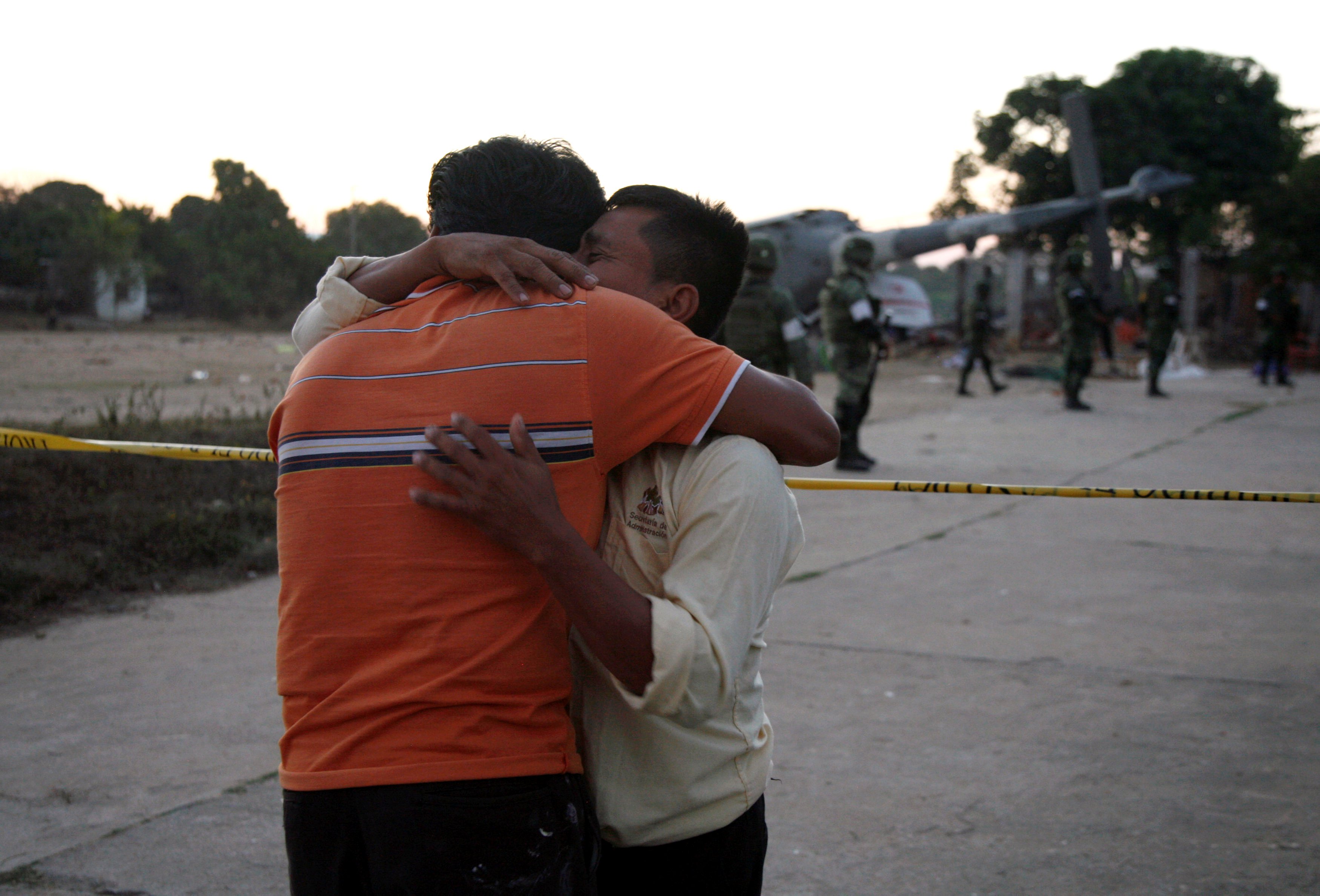 People react as soldiers stand next to a military helicopter, carrying Mexico