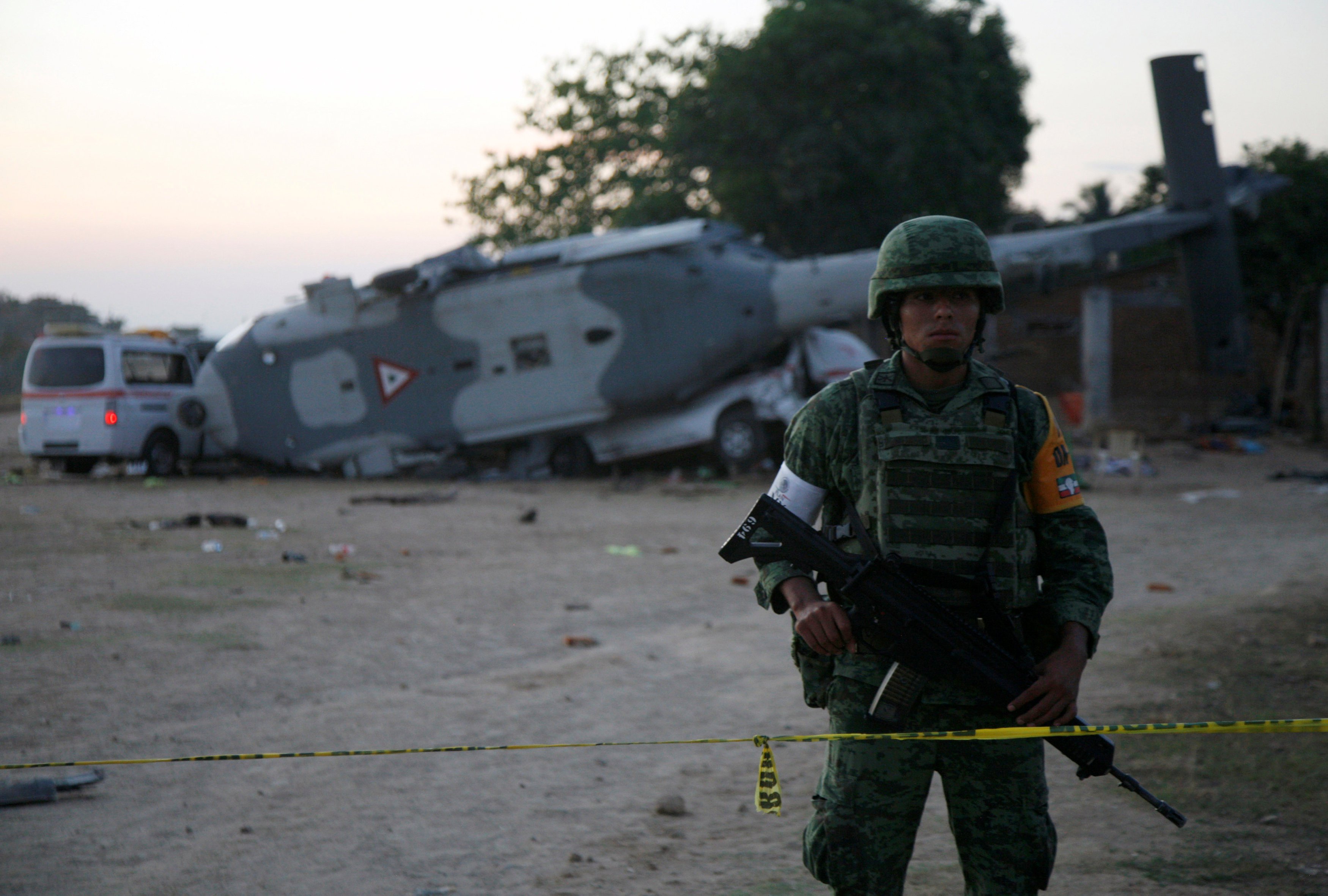 A soldier stands guard next to a military helicopter, carrying Mexico