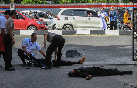 Los espectadores toman fotos mientras la policía examina los cuerpos de dos atacantes después de lanzar un ataque contra la sede de la policía en Pekanbaru. Foto: AFP