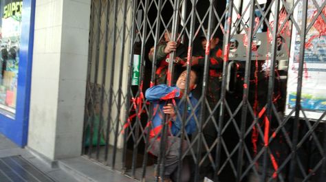 Un funcionario de Bolivia Tv se aferra a la reja para impedir que ingresan los estudiantes de la UPEA.