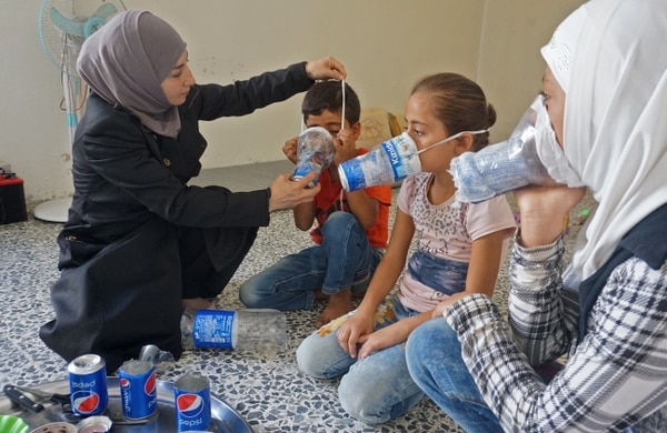 Una mujer improvisa unas máscaras de gas con botellas de plástico para proteger a sus hijos (AFP PHOTO / Muhammad HAJ KADOUR)