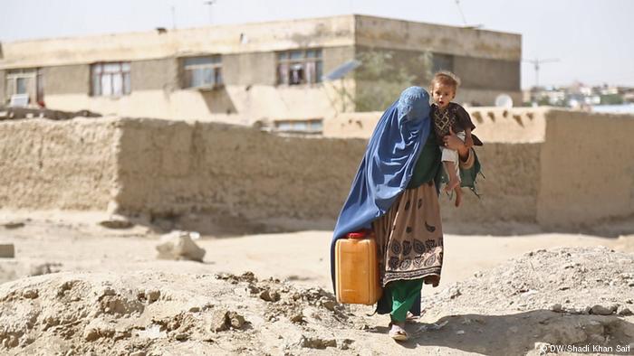 Una mujer transportando un bidÃ³n de agua en una mano y un niÃ±o en la otra.