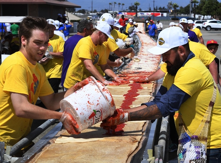 Voluntarios esparcen salsa de tomate y queso en la base de la pizza mientras rompen con éxito el premio Guinness World Records para la pizza más larga con una longitud de 2,13km en la pista del Auto Club Speedway, en Fontana, California el 10 de junio de 2017. Un consorcio de fabricantes de hornos de pizza y panaderos unieron sus fuerzas para romper el récord anterior que ostentaba el Nápoles en Italia por 182 metros. (AFP)