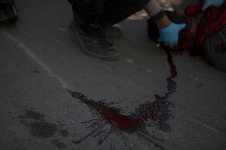 Investigadores revisan un cadáver hallado en la calle, asesinado de un disparo (AP)