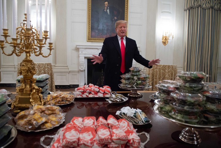 Donald Trump da la bienvenida a los deportistas frente a un banquete de hamburguesas y pizzas. AFP