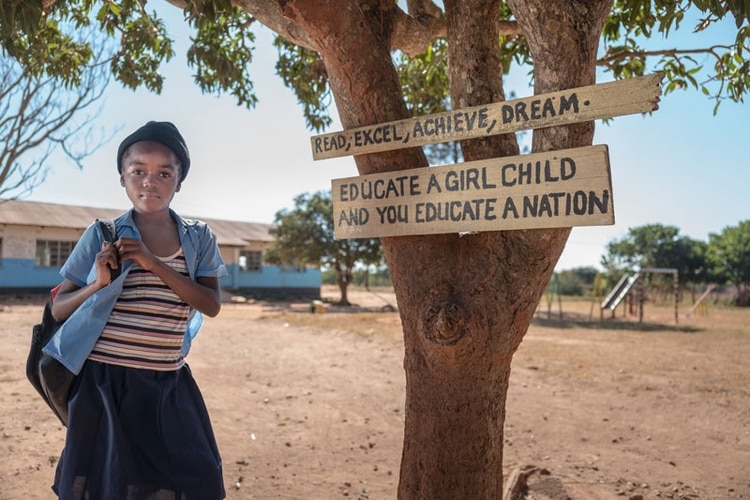 Una estudiante de primaria en Zambia. En el árbol, la leyenda “Lee, destácate, ten éxito, sueña. Educa a una niña y educarás un país” (Bill and Melinda Gates Foundation)