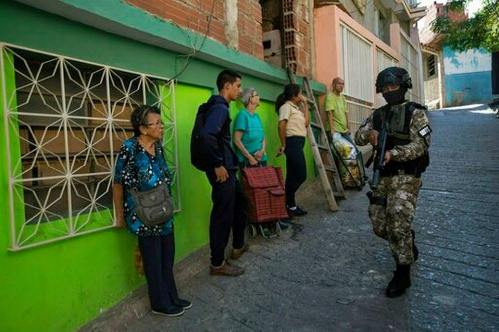 Los residentes se paran cerca de una pared mientras observan a un miembro de la Fuerza de Acción de la Policía Nacional o FAES, Foto: AP