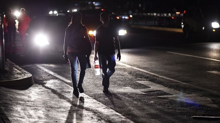 Una pareja camina en una calle oscuras de la ciudad de Caracas (Photo by YURI CORTEZ / AFP)