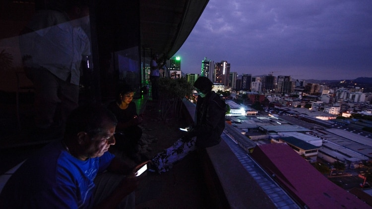 Periodistas iluminados con sus teléfonos durante el apagón en Caracas (Photo by Matias DELACROIX / AFP)