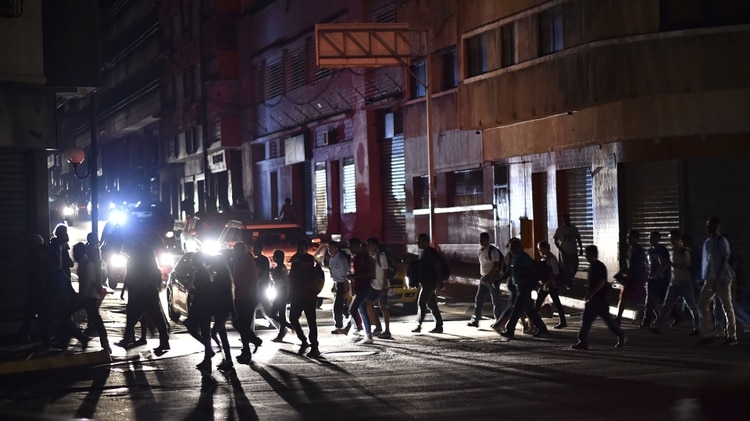 La gente cruza una calle durante un corte de energía en Caracas el 7 de marzo de 2019. – El gobierno de Nicolás Maduro denunció un “sabotaje” contra la principal represa de energía eléctrica en el país, luego de un apagón masivo que dejó a Caracas y vastas regiones de Venezuela en el oscuridad. (Foto por YURI CORTEZ / AFP)