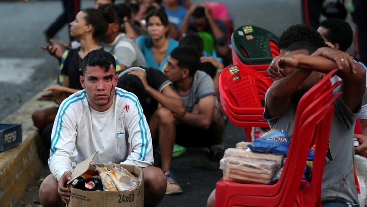Los detenidos esperan a ser registrados por la policía, todavía con los productos que saquearon de un comercio cerrado (REUTERS/Ivan Alvarado)