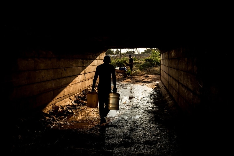 Un grupo de personas recogían agua de una tubería ubicada debajo de un puente en Maracaibo. (Meridith Kohut para The New York Times)
