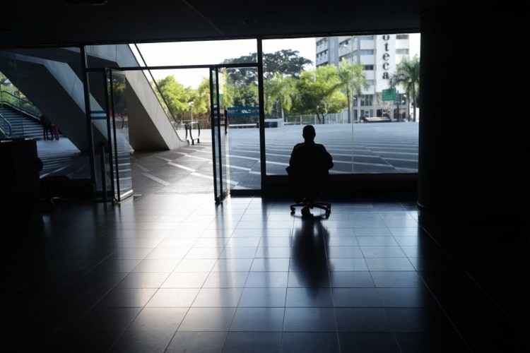 Un hombre mira por la ventana en una oficina sin luz en Caracas (EFE/ Rayner Peña)