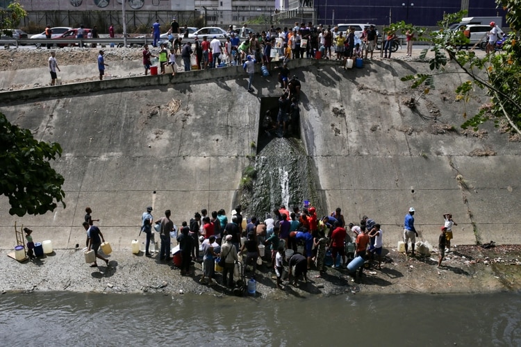 Venezolanos recolectaron agua de un canal de residuos en el río Guaire en Caracas el 11 de marzo de 2019, mientras un apagón masivo afectaba algunas áreas del país (Foto de Cristian HERNANDEZ / AFP)