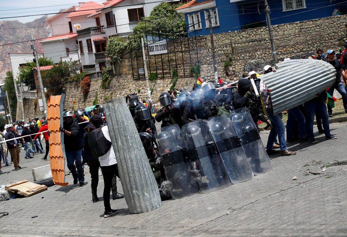 Los policías se cubren en medio de los choques contra los manifestantes detractores de Evo Morales; un uniformado apunta directo a los protestantes (REUTERS/Kai Pfaffenbach)