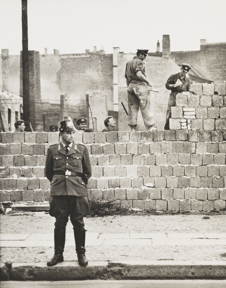 Un policía de Berlín Oeste se para frente al muro de hormigón que divide Berlín Este y Oeste. A lo largo de la calle Bernauer, los obreros de Berlín Este añaden bloques para aumentar la altura de la barrera el 11 de octubre de 1961 (Foto de Everett/Shutterstock (10293355a))