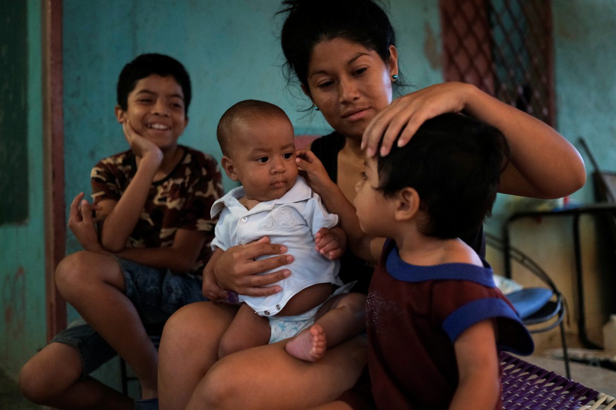 Francys Rivero sostiene a su hijo Kenai, de cinco meses, que se recuperó de la desnutrición, mientras habla con sus hijos Collins, de 11 años, y Enmanuel, de 2, fuera de su casa en Barquisimeto (REUTERS/Carlos Garcia Rawlins)