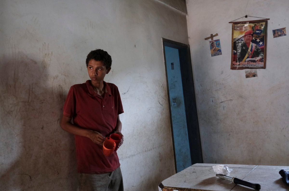 Carlos Flores, de 15 años, que tiene bajo peso por su estatura, según su madre, Blanca Naveda, se para frente a fotos del fallecido presidente de Venezuela, Hugo Chávez, en su casa en Barquisimeto (REUTERS/Carlos García Rawlins)