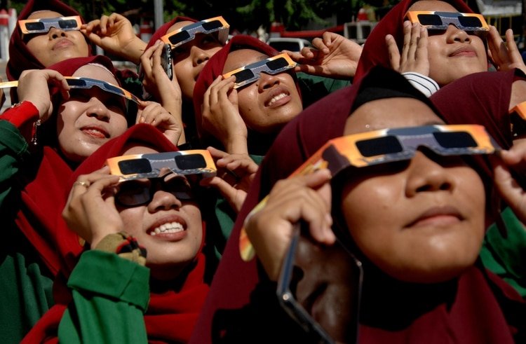 Mujeres usando unas gafas especiales para observar el eclipse (Antara Foto/Abriawan Abhe/via REUTERS)