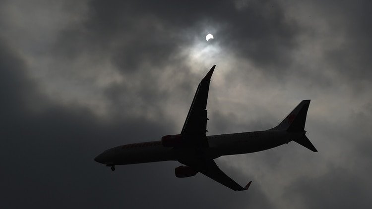 An airplane flies past as the moon moves in front of the sun in a rare 