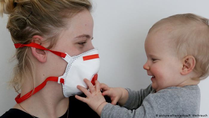 Una mamá utiliza una máscara, mientras toma a su bebé. 