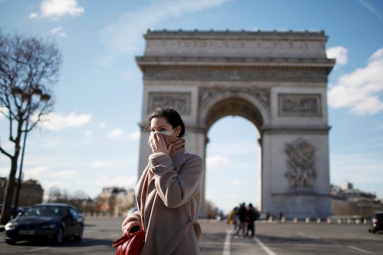 A woman wearing a protective mask, walks near Arc de Triomphe following France